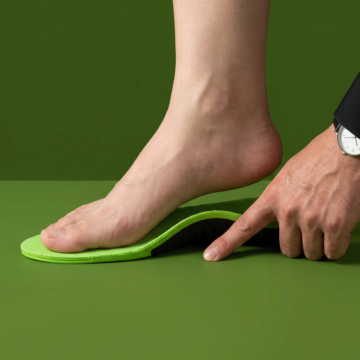 A close-up of a person's foot and hand demonstrating the flexibility and fit of a bright green arch support shoe insert on a solid green background.