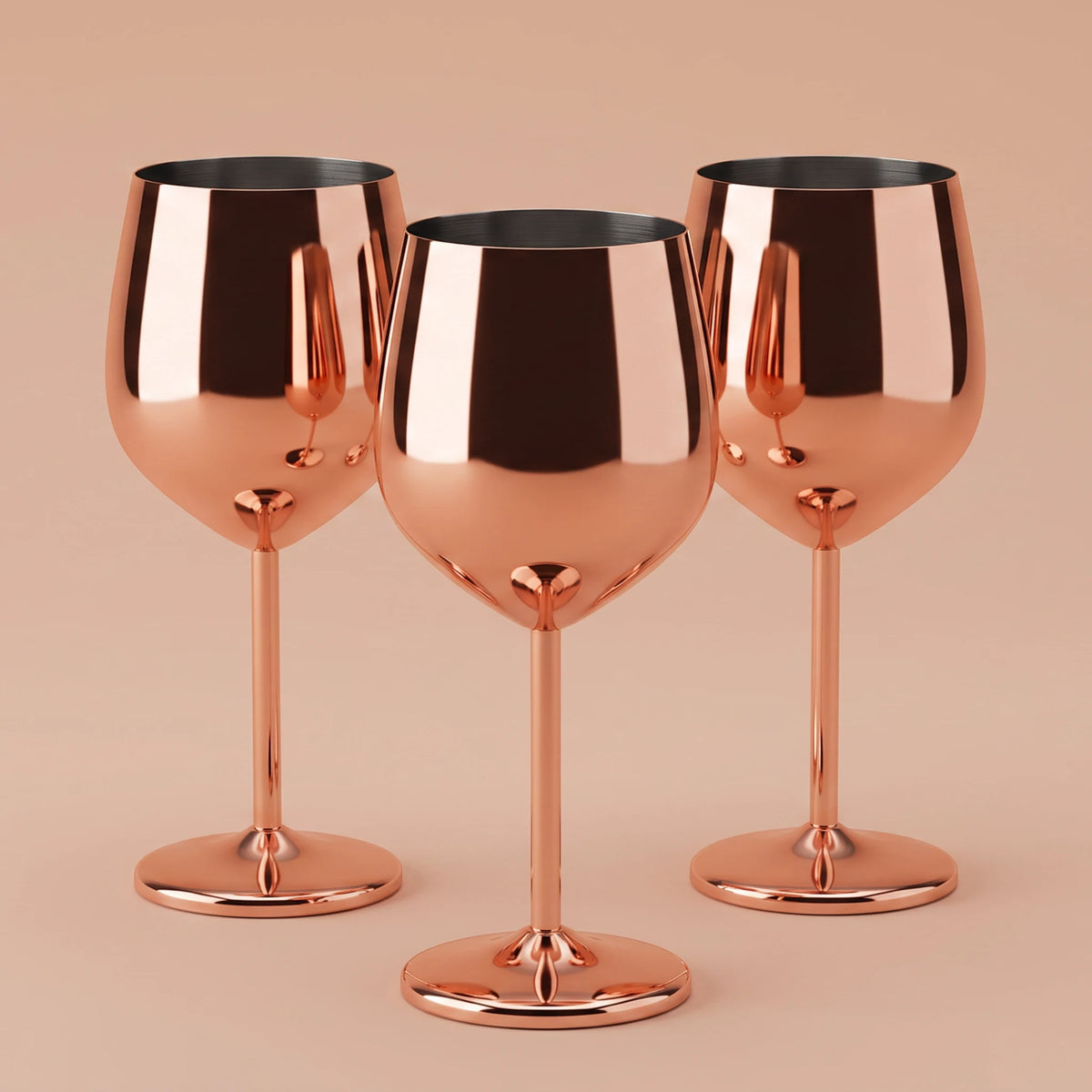 Three metallic rose gold wine glasses arranged together on a solid warm beige background.