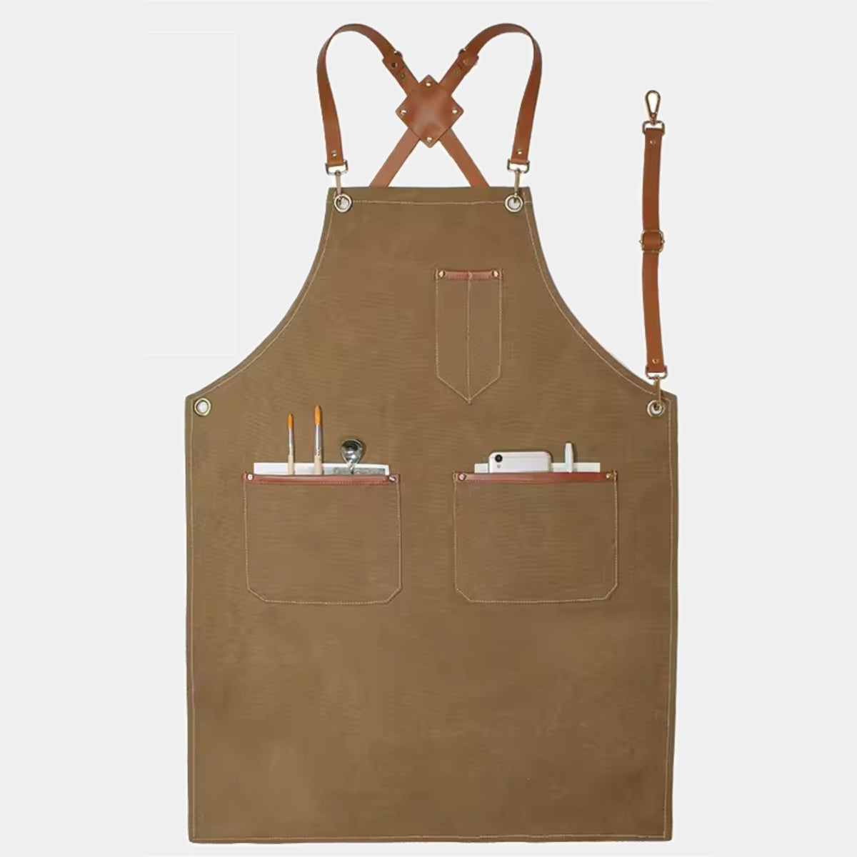 A brown canvas apron with tan leather straps and metal grommets, featuring two front pockets holding art tools, shown against a light gray background.