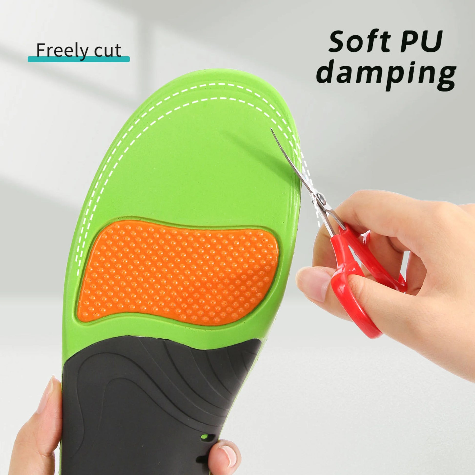 Green and black shoe insole with orange damping pad being cut by red scissors, on a light gray background.