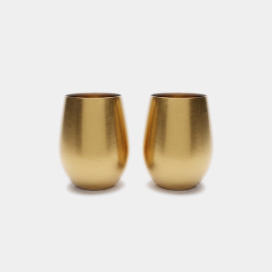 Two small metallic gold cups with a brushed finish, standing side by side on a light gray background.