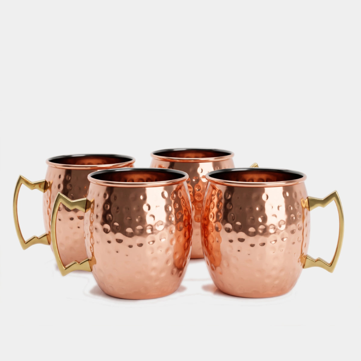 Four hammered copper Moscow mule mugs with gold-toned handles, arranged in a group on a light gray background.